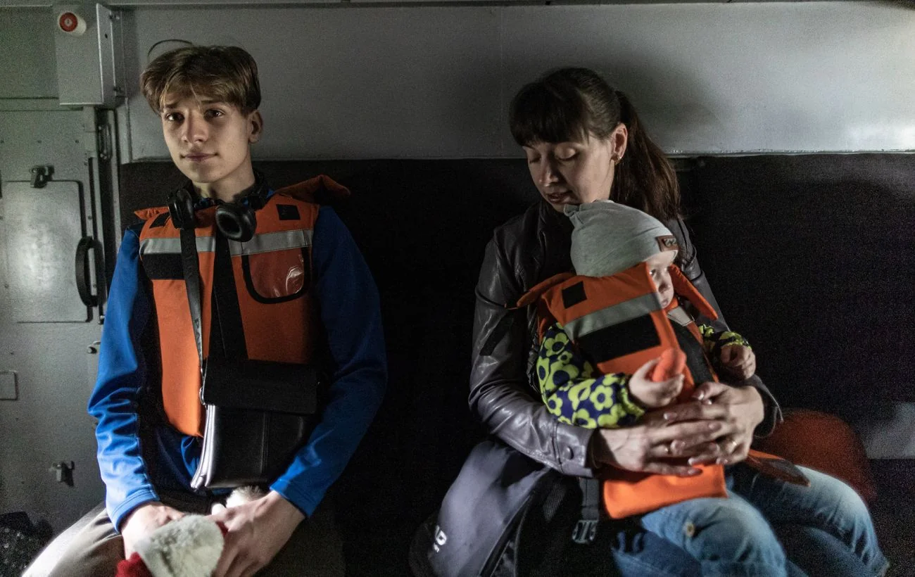 Хлопець і жінка з немовлям у рятувальних жилетах сидять у салоні транспорту