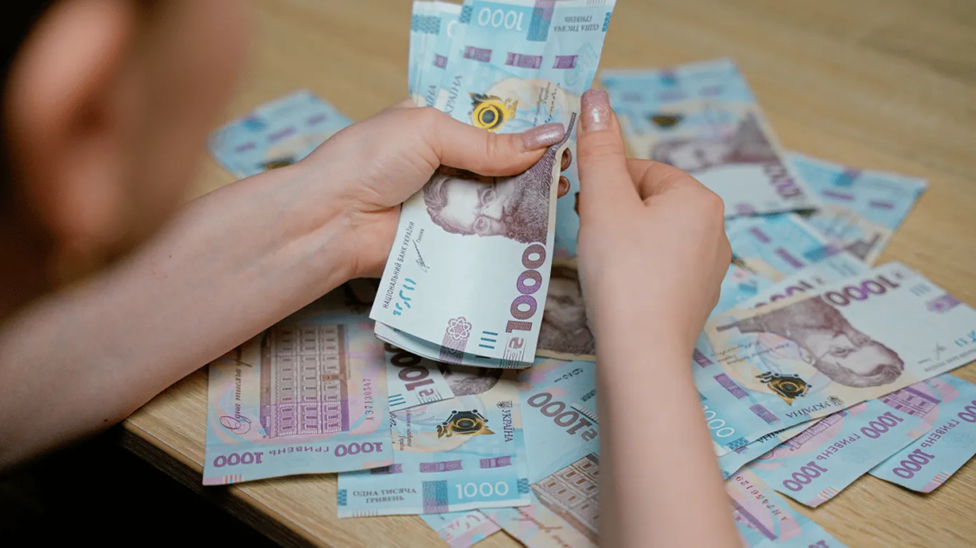 Руки тримають пачки банкнот по 1000 гривень на столі