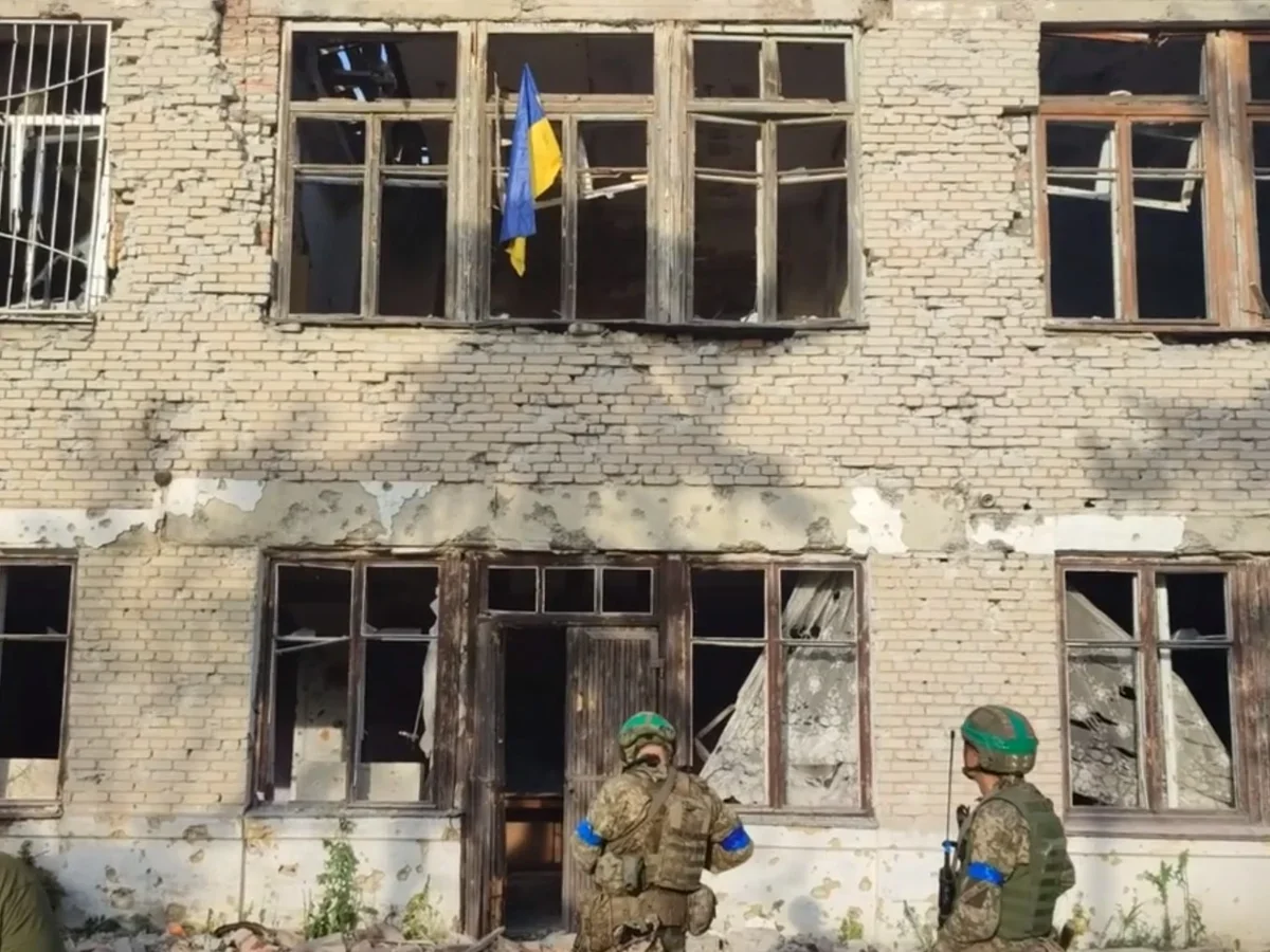 Українські військові біля пошкодженої будівлі з прапором України в Новохатському